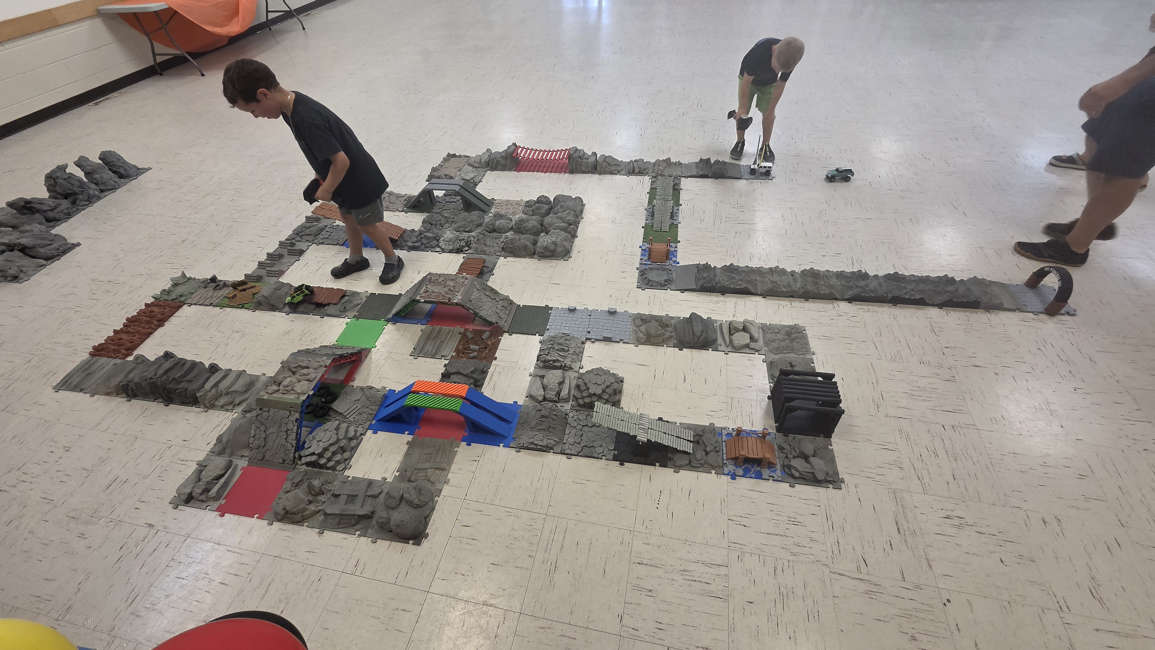 Kids navigating RC crawlers across modular 3D-printed bridges and mountain features